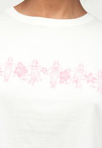 White cotton t-shirt featuring a pink graphic print of hula dancers and hibiscus flowers along the hem. Smooth texture, crew neckline.