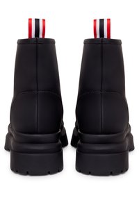 Botas de tobillo de cuero negro con una suela gruesa. Presentan una asa trasera acanalada en rojo, blanco y negro. Detalles de costura visibles.