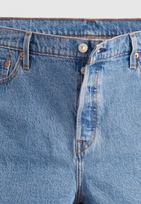 Jean en denim bleu clair avec une coupe droite. Comprend une braguette à boutons, des passants de ceinture et des coutures contrastantes orange.