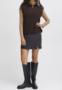 Haut marron côtelé sans manches avec un col zippé, associé à une mini-jupe gris foncé avec une fente latérale et des bottes noires montantes jusqu'aux genoux.