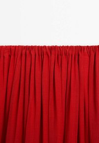 Rideau en tissu rouge froncé avec des plis verticaux espacés régulièrement sur un fond blanc uni.