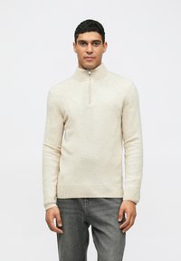 Pull à col zippé beige clair en matériau doux. Présente des manches longues, des poignets et un ourlet côtelés avec un design minimaliste.