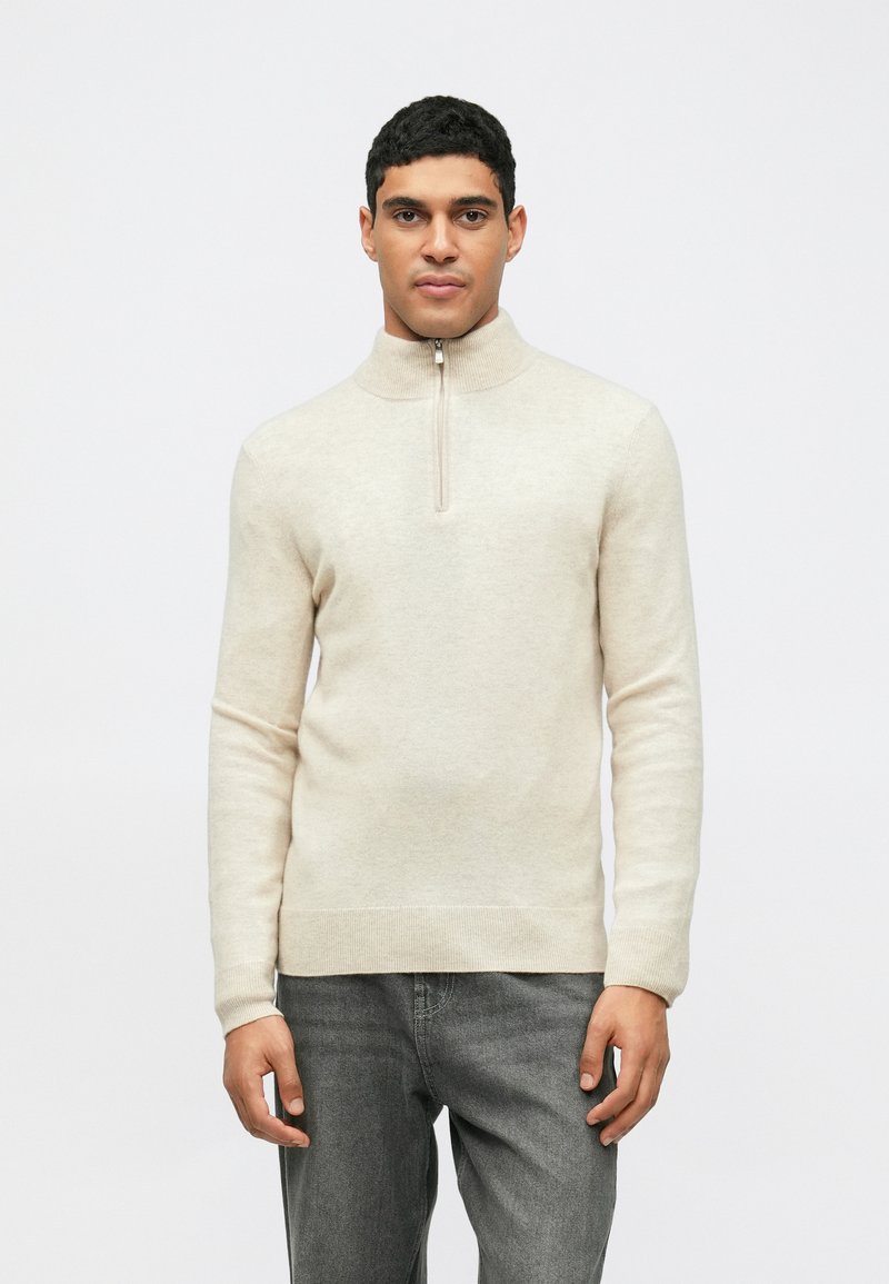 Pull à col zippé beige clair en matériau doux. Présente des manches longues, des poignets et un ourlet côtelés avec un design minimaliste.