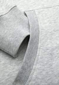 Sudadera gris con una tela suave y texturizada. Presenta un escote redondeado y puños acanalados. Los detalles de las costuras añaden estructura.