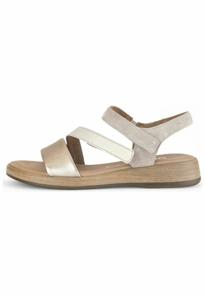 Kevyt sandaali, jossa on metallinhohtoinen kultainen varvastuki, valkoinen ristivyö ja pehmeät harmaat mokka-asusteet. Matala puinen pohja mukavuutta varten.