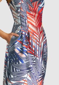 Robe à imprimé tropical avec une silhouette ajustée, tissu lisse, motifs de feuilles rouges et bleues, et poches latérales pour un usage pratique.