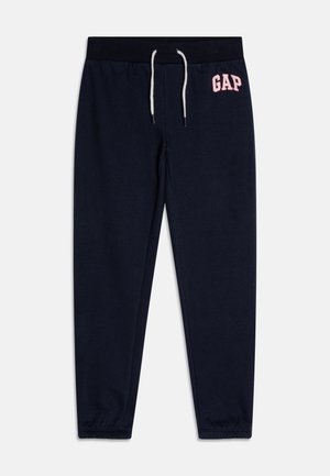 Pantalon de survêtement bleu marine avec taille élastique, cordon blanc, poignets élastiques et logo "GAP" rose sur la partie supérieure de la cuisse gauche.