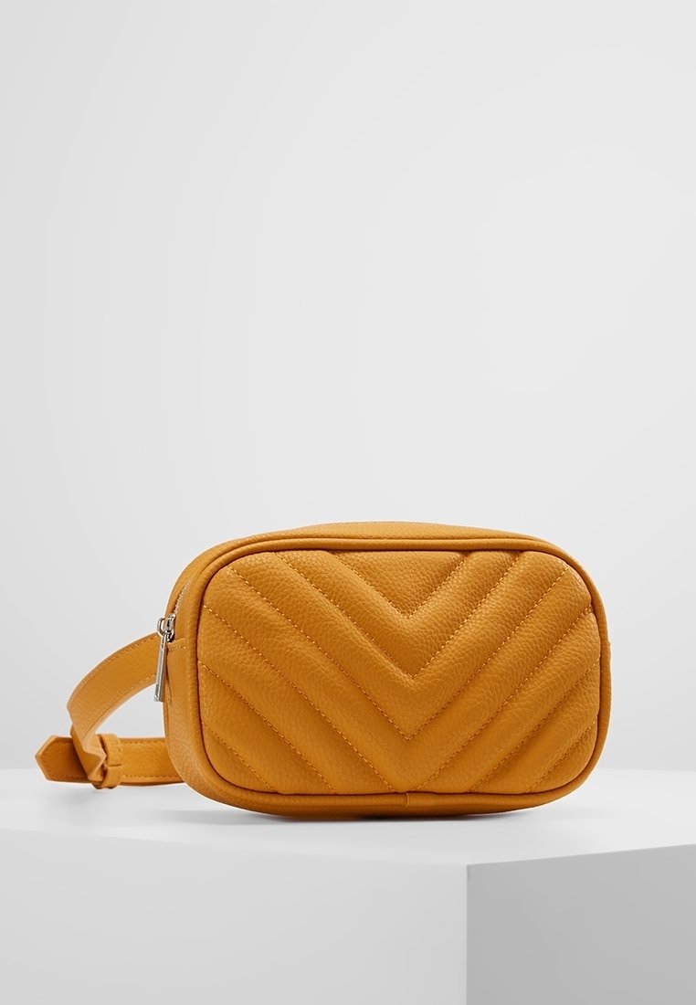 Sac bandoulière en cuir matelassé jaune avec une forme rectangulaire, un motif chevron et une sangle ajustable. Dispose d'une fermeture éclair.