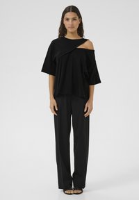 T-shirt noir oversize avec un détail diagonal, associé à un pantalon noir ample. Texture lisse, design minimaliste et manches courtes larges.