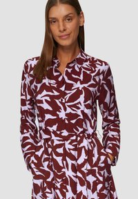Sukienka koszulowa z długim rękawem w bordowym kolorze z białym abstrakcyjnym wzorem, z zapięciem na guziki z przodu, kołnierzykiem i paskiem w talii. Teksturowany materiał z kieszeniami.