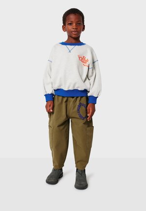 Šedá mikina s modrým límcem a manžetami, oranžové logo; olivové cargo kalhoty s bočními kapsami, modrý kruhový vzor; šedé boty.