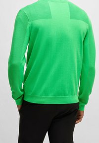 Grön stickad tröja med ribbade axeldetaljer, rundt halsringning och en jämn textur. Bärs med svarta byxor.