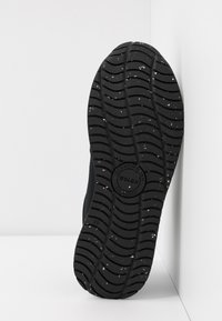 Black sneaker sole with a textured rubber surface, featuring a circular logo and small white speckles throughout the tread pattern.