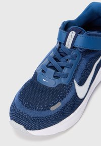 Zapatilla deportiva de punto azul con collar acolchado, logo de swoosh blanco y acentos de plástico. Cuenta con un cierre de cordones y una superficie texturizada.