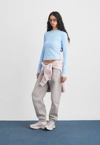 Ανοιχτό μπλε ριγωτό μπλουζάκι μακρύ μανίκι, γκρι φόρμες και ροζ πουλόβερ δεμένο στη μέση, και ανοιχτό ροζ αθλητικά παπούτσια.