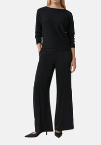 Top lungo a maniche nere e glitterate abbinato a pantaloni neri a gamba larga e tacchi neri a punta. Design semplice e piatto con texture sottile.