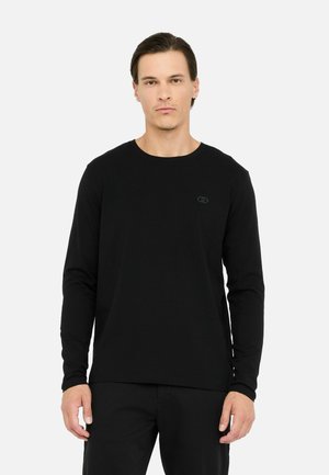 T-shirt a maniche lunghe nera in cotone, con scollo rotondo e un piccolo logo ricamato sul petto, abbinata a pantaloni neri.