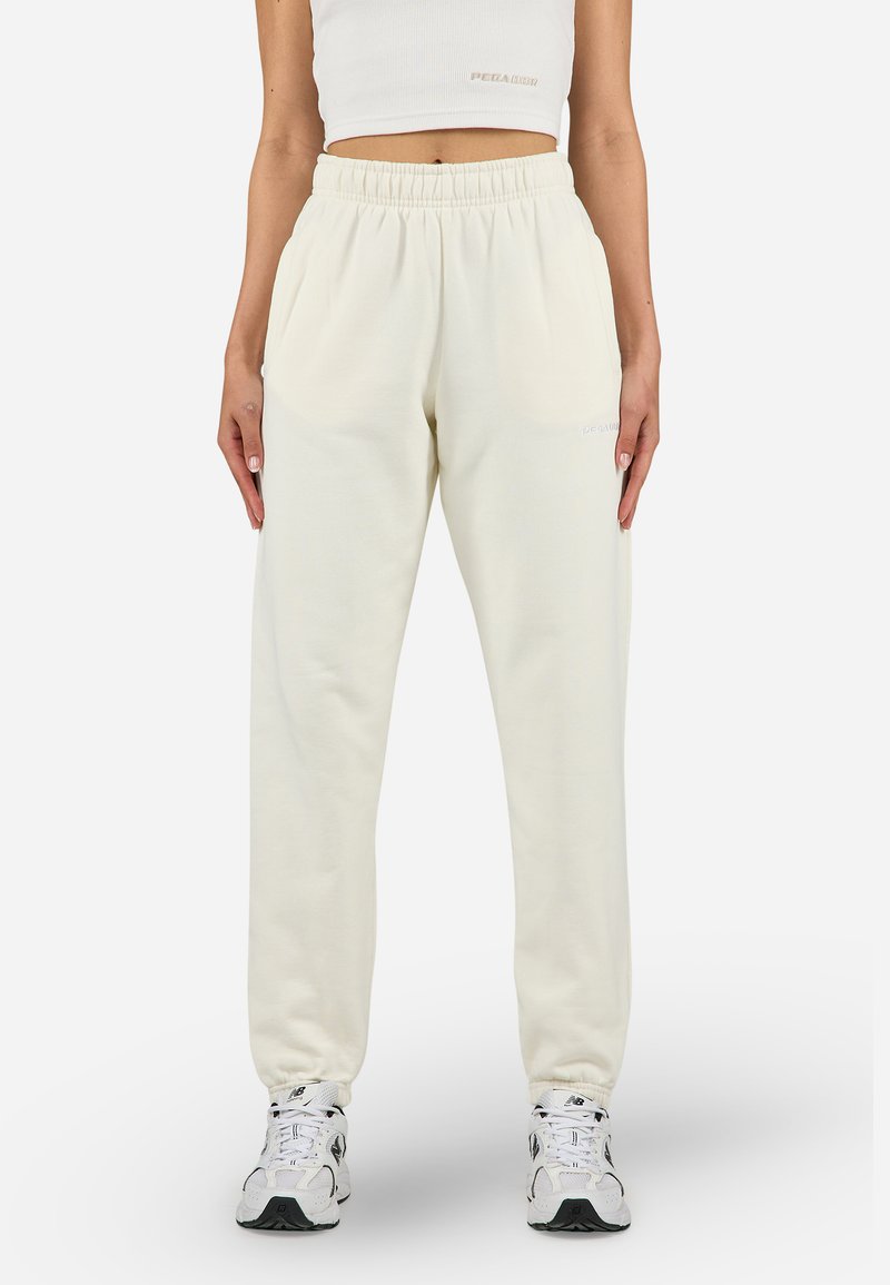 Pantaloni de trening crem cu talie elastică și buzunare laterale, având o textură moale și un detaliu subtil al logo-ului pe coapsă.