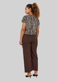 Short-sleeve, zebra-print top in beige and black, paired with brown wide-leg pants. Accessories include hoop earrings and black heeled sandals.