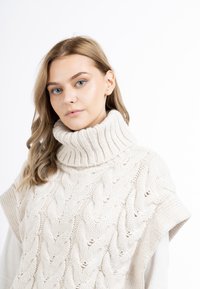 Cremfarbener gestrickter Pullover mit hochfloriger Rollkragen, der ein Kabelstrickmuster und kurze Ärmel aufweist. Sanfte Textur und lockere Passform.