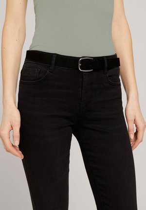Jeans en denim noir avec une coupe slim, accompagnés d'une ceinture en cuir noir avec une boucle en argent. La chemise est vert clair et ajustée.