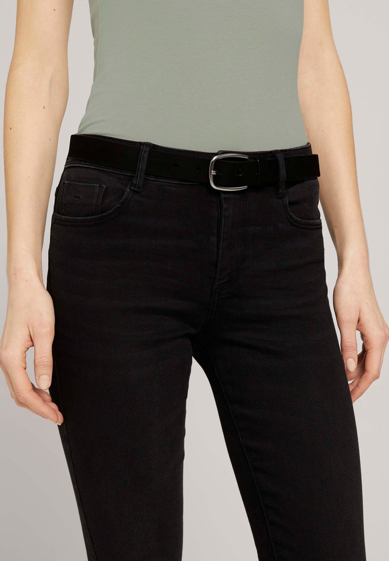 Svarta denimjeans med smal passform, tillsammans med ett svart läderbälte med en silverspänne. Skjortan är ljusgrön och åtsittande.