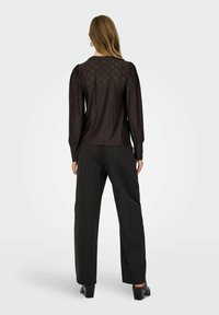 Schwarze Bluse mit langen Ärmeln, gemustertem Textur, gepufften Schultern und Rundhalsausschnitt, kombiniert mit lockeren schwarzen Hosen und klobigen Absatzschuhen.