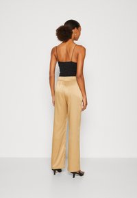 Zwart cropped camisole met spaghettibandjes, gecombineerd met hoge, vloeiende beige broeken. De broeken hebben een gladde, glanzende textuur.