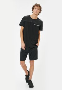 Sort atletisk T-shirt med struktureret øverste del, udstyret med et hvidt logo. Parret med sorte shorts og sorte træningssko.