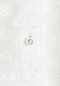 White fabric with embossed floral patterns and a glossy pearl accent attached with a silver fixture. Detailed texture and subtle design.