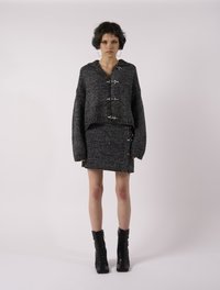 Γκρι πλεκτό κοντό καλοκαίρι με κούμπωμα τύπου toggle, συνδυασμένο με μια ταιριαστή υφασμάτινη μίνι φούστα. Το μοντέλο φοράει μαύρες μποτες με κορδόνια.