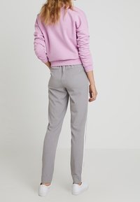 Ljusrosa sweatshirt med ribbade ärmmuddar och nederkant, i kombination med grå slim-fit byxor som har en vit sidostrand och ankellängd.