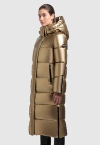 Gouden pufferjack met een lange silhouet, glanzende afwerking, ritszakken aan de zijkant en een capuchon, voorzien van een doorgestikt patroon en een logo op de mouw.