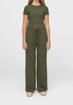 Jeune personne portant un haut à manches courtes côtelé de couleur vert olive et un pantalon à jambes larges avec cordon de serrage, accompagnés de chaussures à plateforme beige.