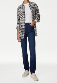 Knapp-up rutig skjorta i svart, vitt och grått över en åtsittande vit ribbad topp, kombinerad med mörkblå raka jeans och beige sneakers.