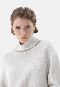 Cremfarbener Strickpullover mit hohem Kragen, der überstrukturierte Muster und einen lässigen Schnitt verfügt. Der Stoff wirkt weich und gemütlich.