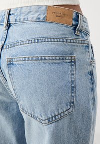 Ανοιχτό γαλάζιο τζιν παντελόνι με ψηλή μέση, πίσω τσέπες και καφέ ετικέτα με την επιγραφή "τέλεια τζιν" και το όνομα της μάρκας ανάγλυφο.