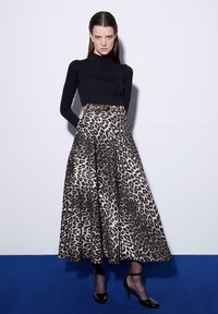 Top nero a maniche lunghe con texture a coste, abbinato a una lunga gonna leopardata con design a campana e cintura in vita. Tacchi neri.
