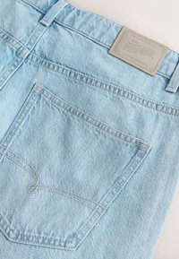 Jeans in denim azzurro chiaro con superficie strutturata, dotati di tasca posteriore e toppa in pelle beige con marchio in rilievo.