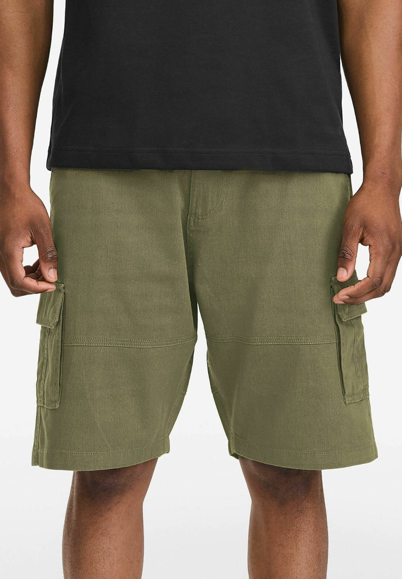 Olive green cargo shorts with two side pockets, a smooth texture, and visible stitching details, paired with a black t-shirt.