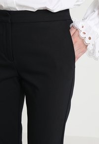 Czarne spodni z dopasowanym krojem i gładką fakturą, z bocznymi kieszeniami. W połączeniu z białą bluzką ozdobioną koronkowym wykończeniem przy rękawach.