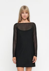 Abito nero con maniche lunghe in trasparenza, scollatura rotonda e corpo aderente. Tessuto liscio, design al ginocchio, stile minimalista.