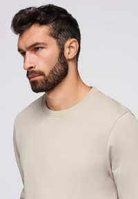 Felpa beige chiaro con scollo rotondo, texture liscia e vestibilità comoda. Presenta polsini a coste e un design pulito e minimalista.