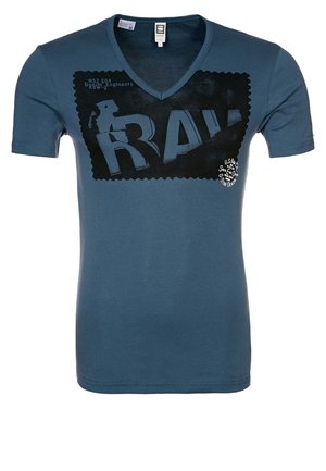 Niebieski T-shirt z dekoltem w kształcie litery V z dużą czarną prostokątną grafiką z napisem "RAW" i małym białym tekstem na piersi.