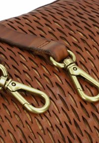 Braune Ledertasche mit Ausstanzmustern, einem glatten Riemen und Beschlägen aus Messing. Die Textur ist glatt mit definierten Formen.