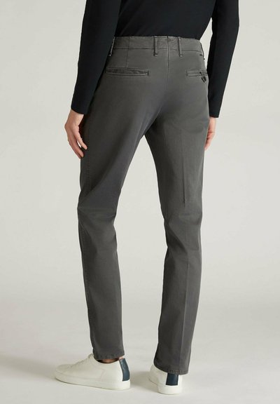 Pantaloni grigi elasticizzati con una vestibilità affusolata, due tasche posteriori e dettagli di cucitura sottili. Indossati con sneakers bianche con un accento scuro.