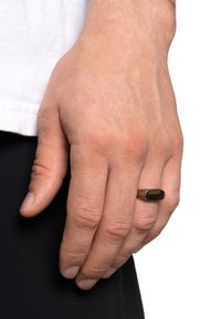Bronzering mit einem rechteckigen schwarzen Stein und einem strukturierten Band. Hand vor einem schlichten Hintergrund gezeigt, mit natürlichen Hauttönen sichtbar.