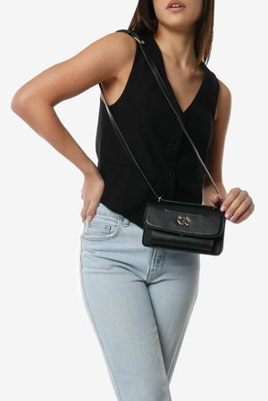 Borsa a tracolla in pelle nera con forma rettangolare, dotata di chiusura magnetica e dettagli in metallo dorato, appesa a una sottile tracolla.