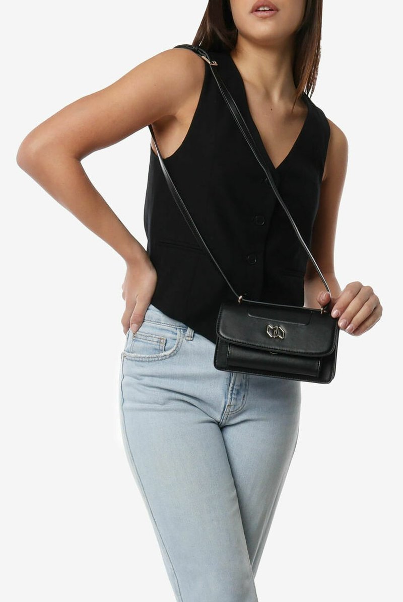 Bolso cruzado de piel negra con forma rectangular, que cuenta con un cierre magnético y detalles en dorado, suspendido de una correa delgada.