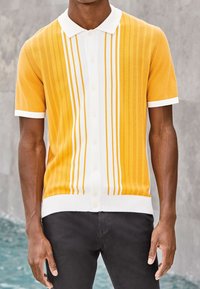 Kurzärmeliges Poloshirt in Orange mit weißen vertikalen Streifen, ausgestattet mit einem klassischen Kragen und weißer Rippbündchen an Ärmeln und Saum.